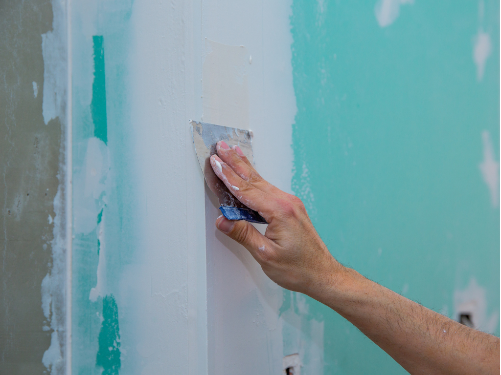 A person applying blue paint to a wall, showcasing the process of home improvement and creativity in action.